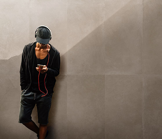 A man leans on tiled wall wearing cap and headphones